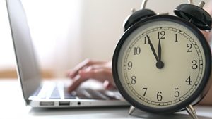 A clock and a person using a laptop in the background