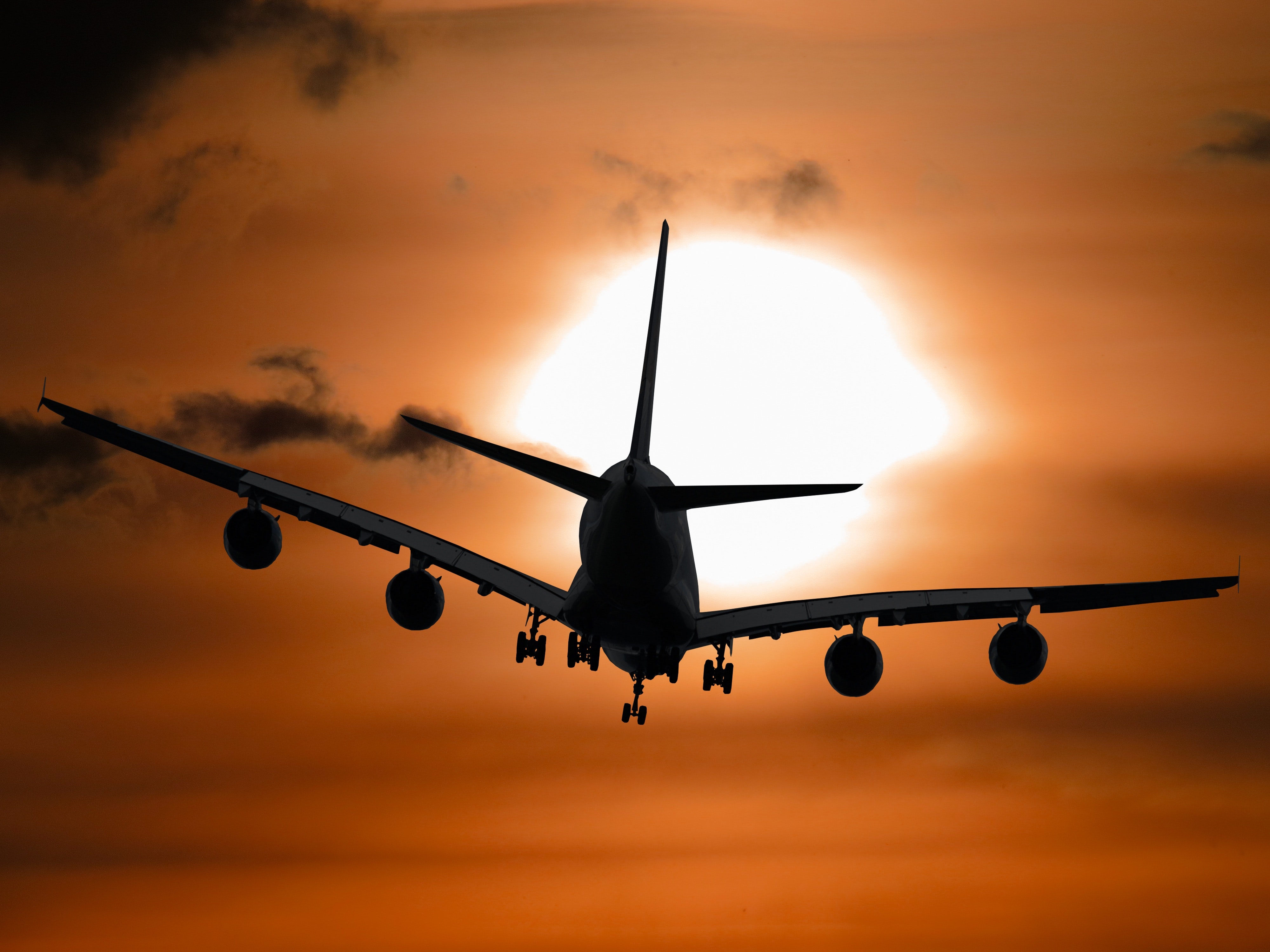 A silhouette of a plane flying in the sky at sunset