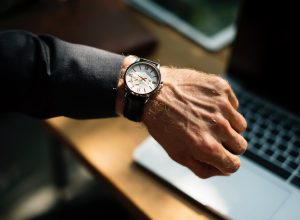 A man's hand with a watch, a laptop in the background