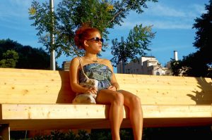 A woman sunbathing on a bench, trees in the background